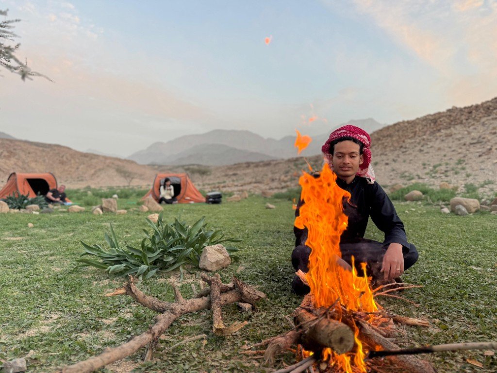 Local guide tending a morning campfire beside the tents